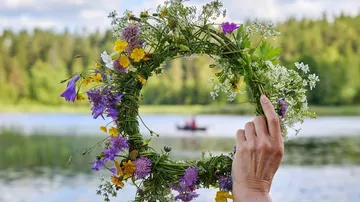 Blumenkranz in Hand, gehalten vor einem ruhigen See.